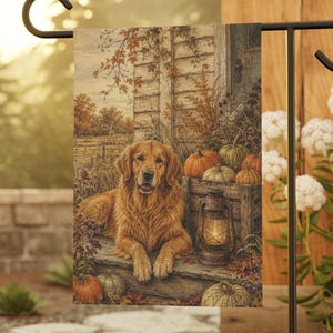 May include: A rectangular garden flag featuring a golden retriever lying on wooden steps. The scene includes a lit lantern, several pumpkins, and autumn foliage against a rustic wooden wall. The flag hangs from a black metal garden stake.