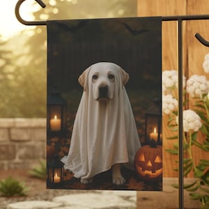 May include: A Halloween garden flag featuring a Labrador Retriever dressed as a ghost. The dog is draped in a white sheet, with a carved pumpkin and lit lanterns in the background. Bats are silhouetted against a dark backdrop.
