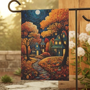May include: A colorful garden flag with a whimsical illustration of a small town at night. The flag features houses with lit windows, trees with fall foliage, and a winding path leading to the center of the town. The flag is displayed on a black metal stand.