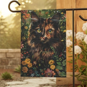 May include: A garden flag featuring a close-up of a calico cat with green eyes surrounded by colorful flowers.