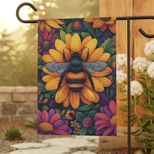 May include: A garden flag with a bee and flowers. The bee is yellow and black with wings. The flowers are yellow, pink, and purple. The background is dark blue.