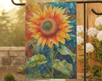 May include: A garden flag featuring a vibrant watercolor sunflower. The sunflower has bright yellow petals, a green center, and a long green stem with leaves. The background has a mix of blue, orange, and brown colors. The flag is displayed on a black metal stand.