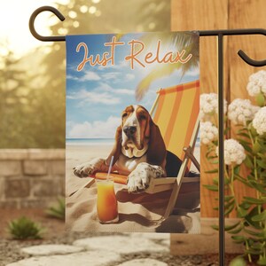May include: A garden flag with a basset hound relaxing on a beach chair with a tropical drink. The flag reads "Just Relax".