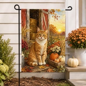 May include: A rectangular garden flag featuring an orange tabby cat sitting on a wooden porch in front of a red barn. The scene includes hay bales, autumn leaves, pumpkins, and potted chrysanthemums under a sunset sky with golden light.