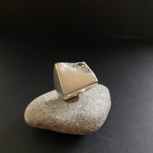 May include: A silver ring with a geometric design and three small brown gemstones.