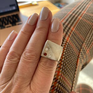 May include: A silver ring with a rectangular face set with three stones. Two of the stones are orange and one is white.