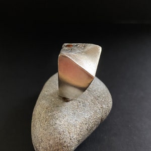 May include: A silver ring with a geometric design and two small red stones set into the top.