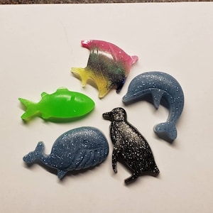 May include: Five colorful resin sea creature figurines. A green fish, a blue whale, a blue dolphin, a black penguin, and a multi-colored fish.