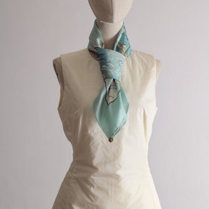 May include: A white sleeveless top with a light blue silk scarf tied around the neck. The scarf has a blue and white floral pattern.
