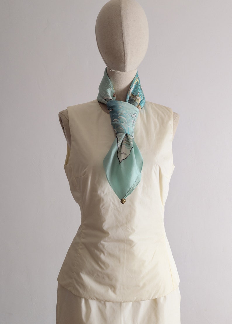 May include: A white sleeveless top with a light blue silk scarf tied around the neck. The scarf has a blue and white floral pattern.