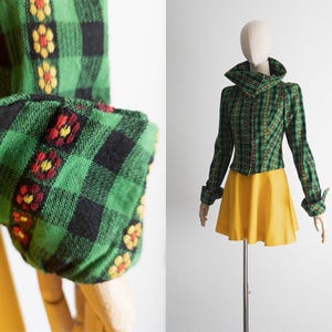 May include: A vintage green and black plaid jacket with floral embroidery on the cuffs and collar. The jacket is paired with a yellow skirt. The jacket is displayed on a mannequin.