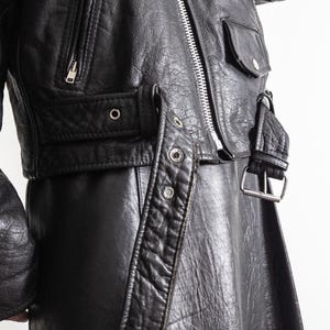 May include: Black leather jacket with a silver zipper, pockets, and belt details. The jacket has a classic biker style with a cropped length and a textured finish. The jacket features a silver buckle and metal rivets.