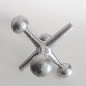 K&ouml;nnte beinhalten: Eine silberfarbene Metallskulptur in Form eines Springerspiels mit sechs strahlenf&ouml;rmigen Armen, die in glatten, kugelf&ouml;rmigen Enden auslaufen. Das Objekt hat eine matte, geb&uuml;rstete Metalloberfl&auml;che und eine zentrale Nabe, von der die Arme ausgehen.