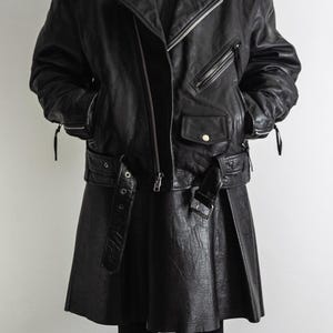 May include: Black leather biker jacket with a matching skirt. The jacket features a diagonal zipper, multiple pockets, and a belted waist. The skirt is a flared style with a buckle belt. The outfit is completed with black leggings.