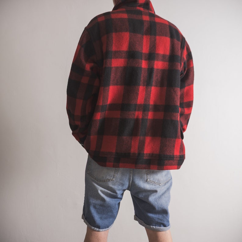 May include: A red and black checked flannel shirt with a collared neckline and long sleeves. The shirt is worn over a pair of blue denim shorts.