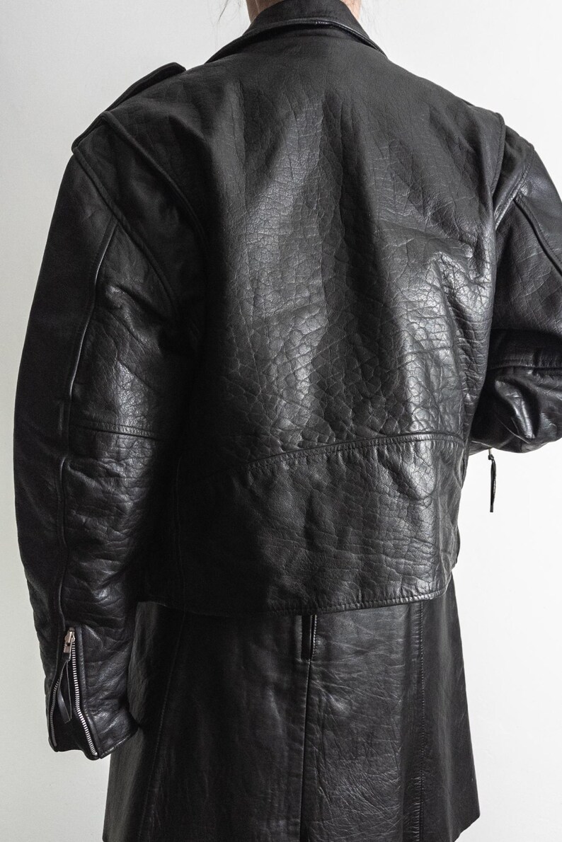 May include: Black leather jacket with a textured finish. The jacket features a classic design with a notched collar, shoulder epaulets, and zippered sleeves. The garment appears to be vintage or pre-owned.