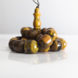 Op de afbeelding: Een witte keramische mok met een zwart handvat en de tekst "But First, Coffee" in een vetgedrukte, zwarte letter. De mok staat op een houten oppervlak. De mok is ongeveer 10 cm hoog.