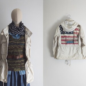 Puede incluir: Un maniquí exhibe un atuendo en capas: una chaqueta beige claro, una bufanda estampada, una camisa vaquera, un suéter verde y marrón y una falda vaquera. Una segunda imagen muestra una chaqueta crema con un diseño de la bandera estadounidense en la espalda.