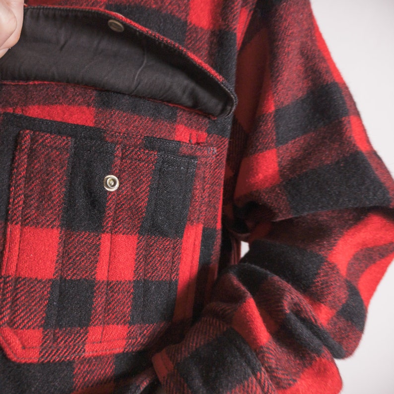 May include: Red and black checked flannel shirt with a large pocket on the front. The shirt has a button-up closure and a relaxed fit.