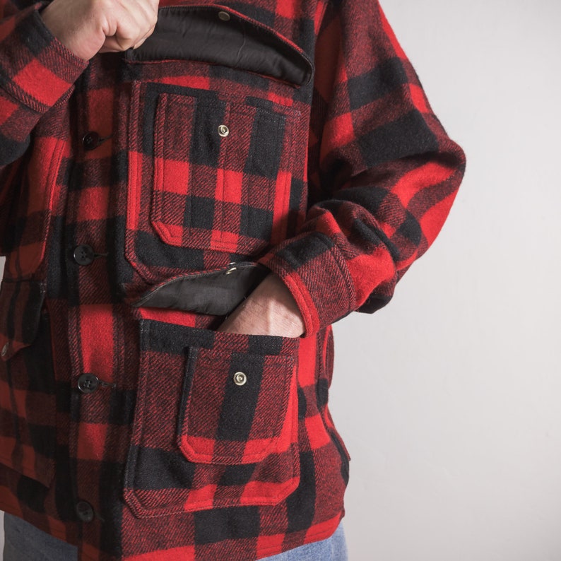 May include: A red and black checked flannel shirt with multiple pockets. The shirt has a button-up front and long sleeves.