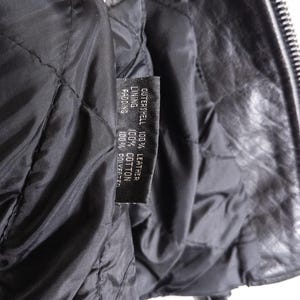 May include: Close-up of the inside of a black leather jacket. The quilted lining is visible, along with a tag indicating the outer shell is 100% leather, the lining is 100% cotton, and the padding is 100% polyester.