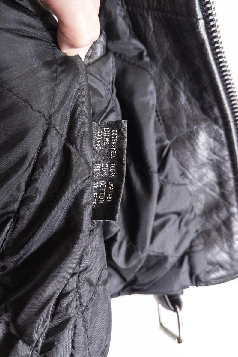 May include: Close-up of the inside of a black leather jacket. The quilted lining is visible, along with a tag indicating the outer shell is 100% leather, the lining is 100% cotton, and the padding is 100% polyester.