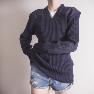 May include: A dark blue knitted sweater with a v-neck and elbow patches. The sweater is made of a thick, textured yarn and has a relaxed fit.