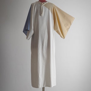 Op de afbeelding: Een witte, beige en blauwe kleurblokjurk met een strik aan de hals. De jurk heeft een losse pasvorm en is gemaakt van een lichtgewicht stof.