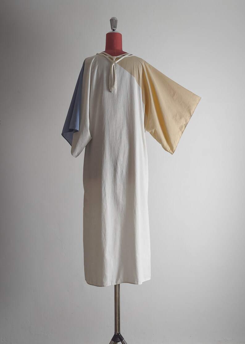 Op de afbeelding: Een witte, beige en blauwe kleurblokjurk met een strik aan de hals. De jurk heeft een losse pasvorm en is gemaakt van een lichtgewicht stof.
