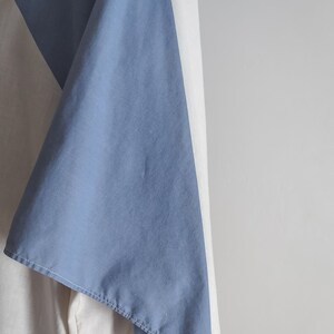 Op de afbeelding: Een blauwe en witte stof met een diagonale naad. De stof is gevouwen en gedrapeerd over een wit oppervlak.