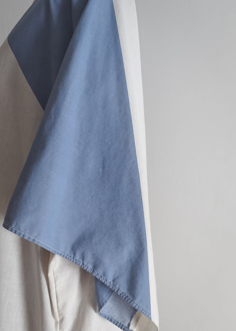 Op de afbeelding: Een blauwe en witte stof met een diagonale naad. De stof is gevouwen en gedrapeerd over een wit oppervlak.