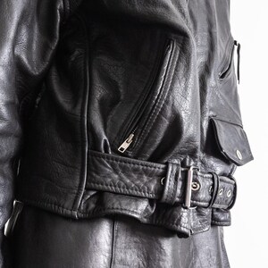 May include: Black leather jacket with a zippered front, multiple pockets, and a belted waist. The jacket has a classic biker style with a silver buckle and zipper details. The leather appears worn, adding to its vintage appeal.