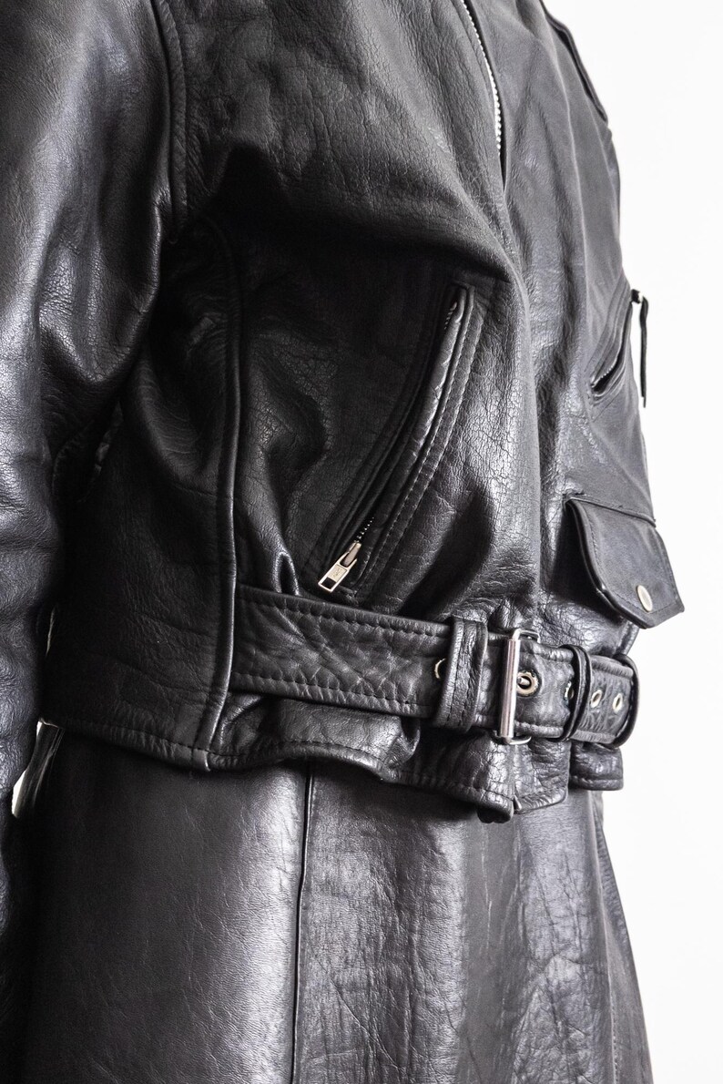 May include: Black leather jacket with a zippered front, multiple pockets, and a belted waist. The jacket has a classic biker style with a silver buckle and zipper details. The leather appears worn, adding to its vintage appeal.