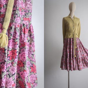 Peut inclure: Une robe à imprimé floral rose et rouge avec un lien à glands jaune. La robe a un corsage smocké et une jupe à volants.