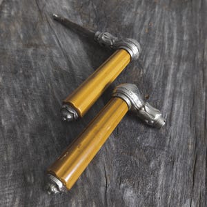 May include: Two antique door handles with a yellow amber finish and silver accents. The handles are made of metal and have a decorative design.