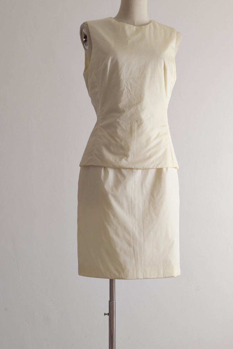 May include: A sleeveless, ivory-colored dress with a fitted bodice and a slightly flared skirt.