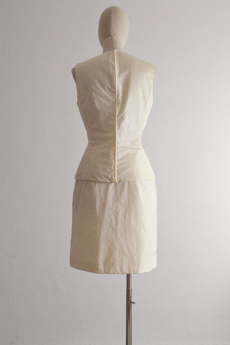 May include: A sleeveless dress in a pale yellow color. The dress has a fitted bodice and a full skirt. The dress is on a mannequin.