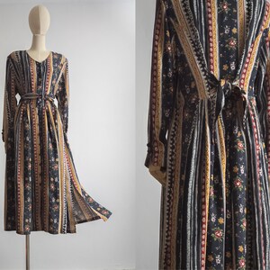 May include: A long-sleeved dress with a black, white and gold striped pattern and floral print. The dress has a tie at the waist and a slit in the skirt.