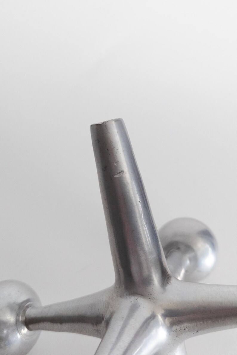 K&ouml;nnte beinhalten: Eine silberfarbene Metallskulptur in Form eines Springerspiels mit einem zentralen Knotenpunkt und sechs strahlenf&ouml;rmigen Armen, die jeweils in einer glatten, kugelf&ouml;rmigen Kugel enden. Die Metalloberfl&auml;che ist matt mit subtilen Lichtreflexen.
