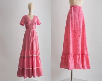 May include: A pink maxi dress with a white floral print and a white button-up front. The dress has a tiered skirt with white trim.