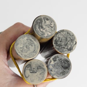 May include: Five cylindrical rods bundled together with a bright yellow rubber band. Each rod features a circular end cap with a marbled pattern of swirling black, gray, and off-white colors, creating a distinct and complex visual texture on every piece.