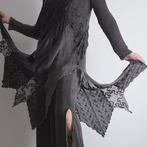 Può includere: Abito grigio scuro a maniche lunghe con design asimmetrico. L'abito presenta dettagli in pizzo e uno spacco alto sul lato. Il tessuto sembra essere una maglia morbida, adatta alla stratificazione. L'abito è lungo circa 150 cm.