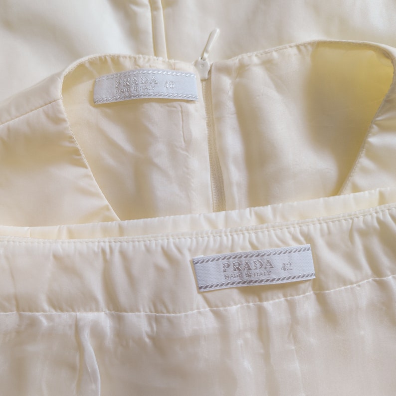May include: Two white fabric labels with black text. The top label reads "PRADA MADE IN ITALY 42". The bottom label reads "PRADA MADE IN ITALY 42".