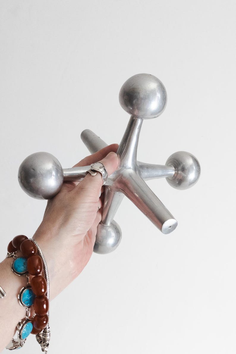 K&ouml;nnte beinhalten: Ein gro&szlig;es, silberfarbenes Metall-Spielzeug in Form eines Springers mit sechs strahlenf&ouml;rmigen Armen, die in glatten, abgerundeten Kugeln enden. Das Objekt hat eine matte, metallische Oberfl&auml;che und eine geometrische Struktur.