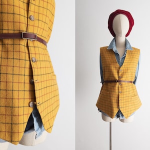 Pode incluir: Colete xadrez amarelo mostarda com cinto de couro castanho. O colete tem fecho de botões e dois bolsos. Uma cabeça de manequim usa uma boina bordô. O colete é sobreposto a uma camisa jeans.
