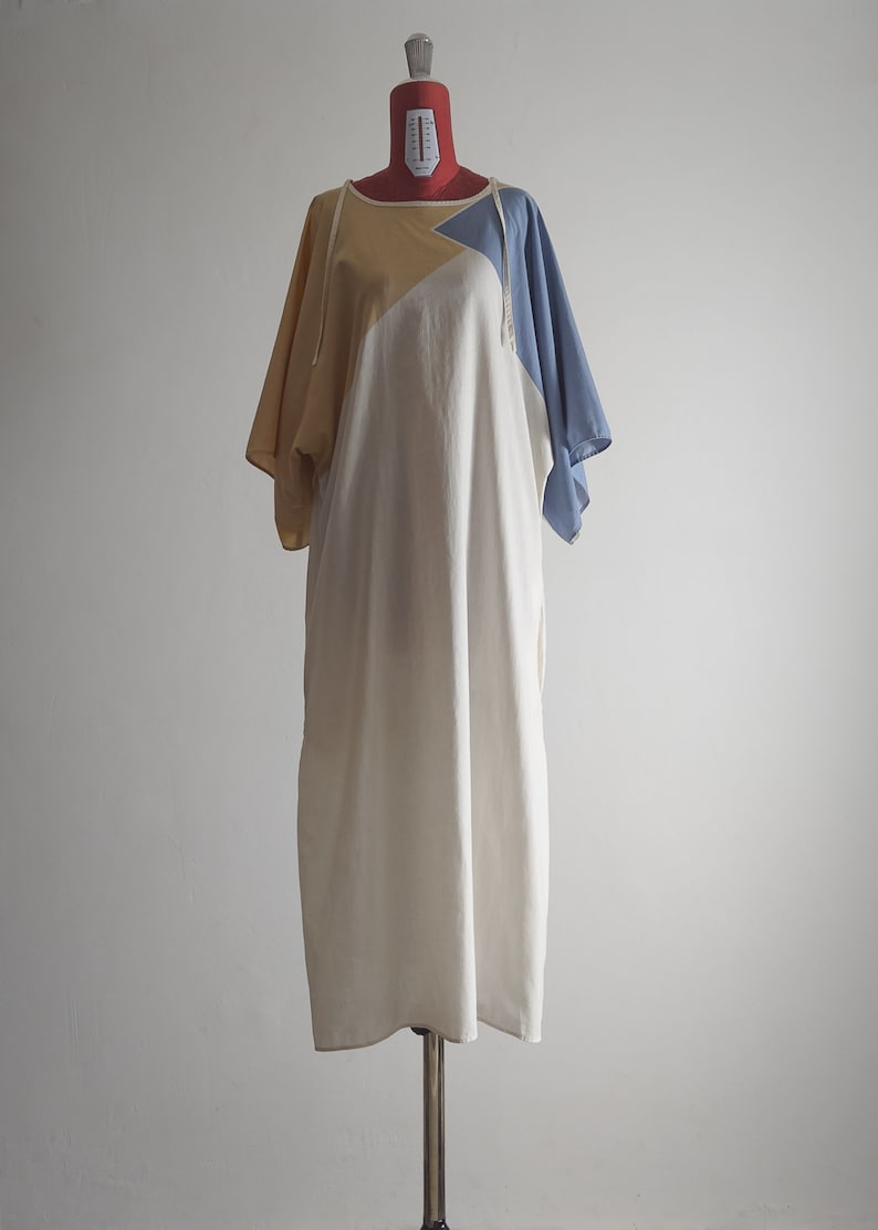 Op de afbeelding: Een witte, gele en blauwe katoenen jurk met een losse pasvorm en korte mouwen. De jurk heeft een eenvoudig ontwerp en is perfect voor een casual look.