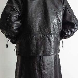 May include: A black leather jacket and skirt set. The jacket has a textured finish, shoulder pads, and a short, cropped design. The skirt is a-line and reaches the mid-thigh. The outfit is displayed against a plain white background.