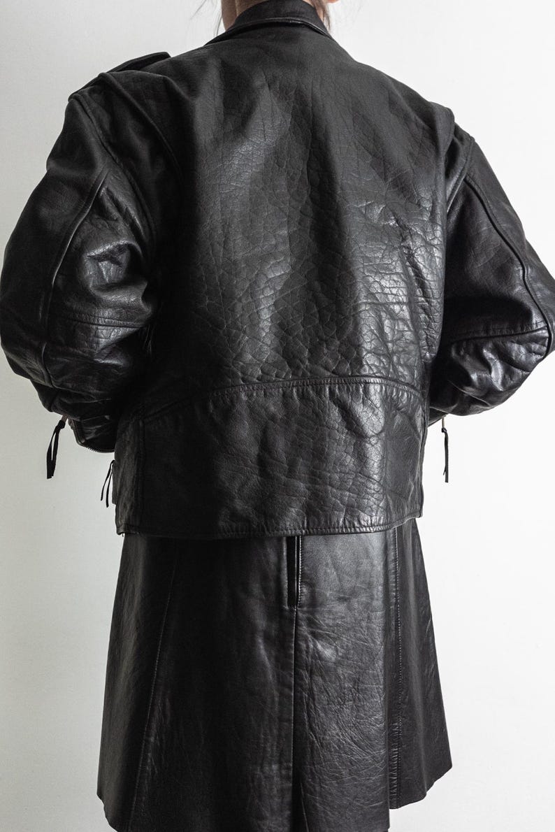 May include: A black leather jacket and skirt set. The jacket has a textured finish, shoulder pads, and a short, cropped design. The skirt is a-line and reaches the mid-thigh. The outfit is displayed against a plain white background.