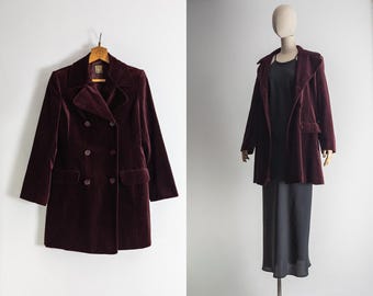 Op de afbeelding: Een bordeauxrode fluwelen double-breasted blazer met een reverskraag en twee voorzakken. De jas wordt op een houten hanger getoond. De tweede afbeelding toont de blazer op een mannequin.