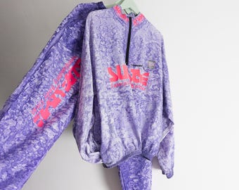 May include: A purple and white marble-patterned tracksuit featuring a quarter-zip pullover with a high collar and long pants. The pullover displays the neon pink text "SURGE" on the chest and "Clearwater" above it, with matching pink text on the pant leg.